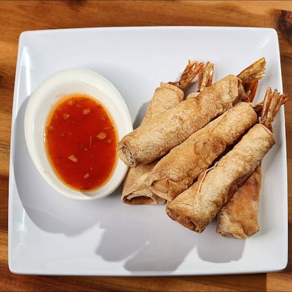Crispy Vietnamese shrimp spring rolls with visible tails, served with a side of sweet chili dipping sauce.