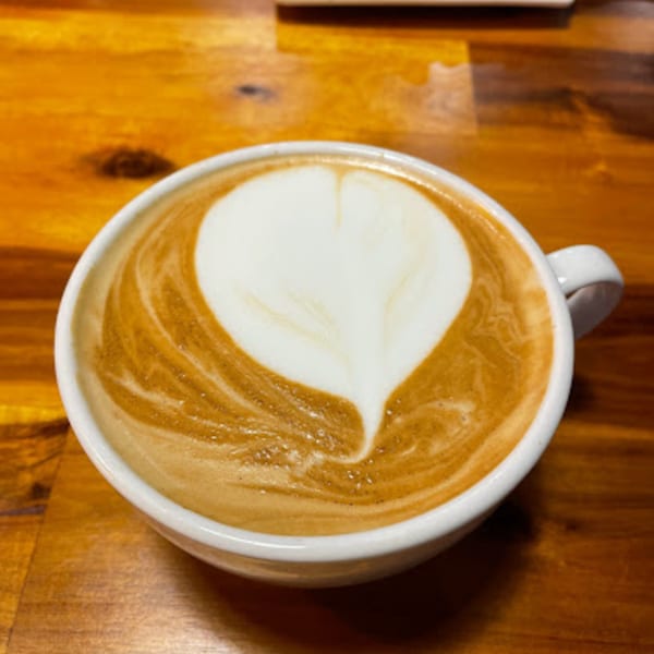 A white cup of latte with a heart-shaped foam design sits on a wooden table.