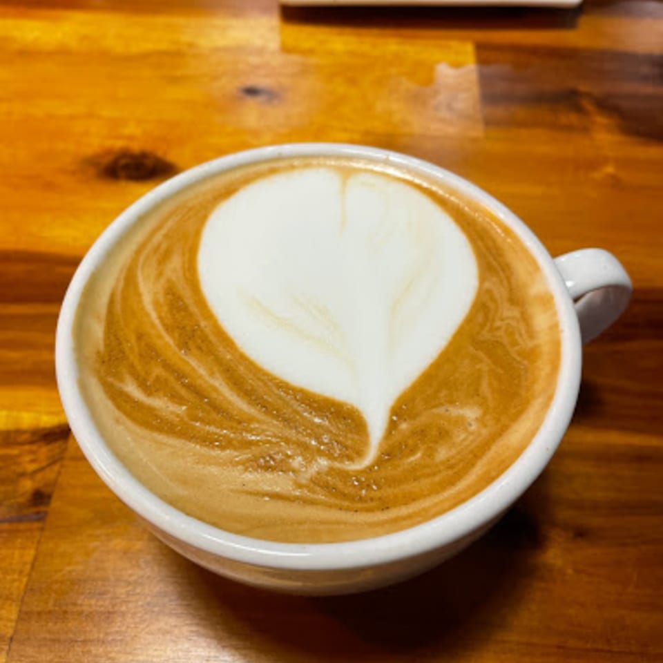 A white cup of latte with a heart-shaped foam design sits on a wooden table.