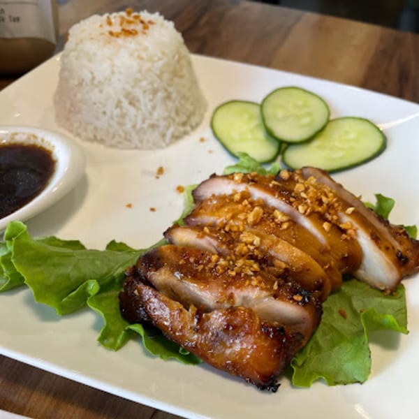 Vietnamese grilled chicken with rice, cucumbers, and dipping sauce on a white plate.