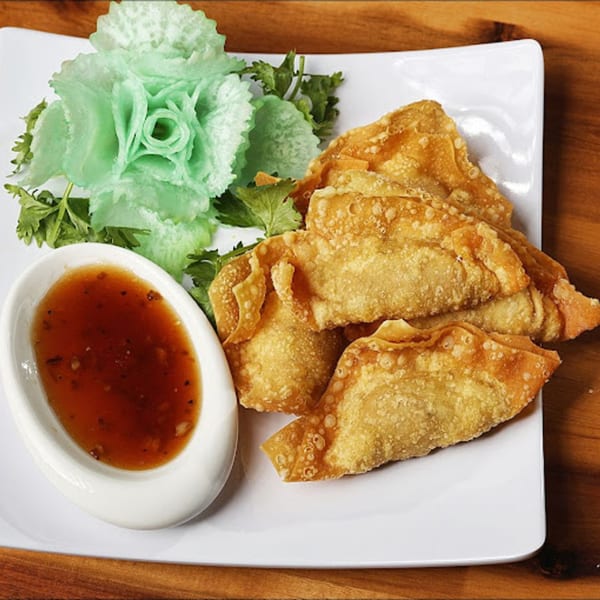 Crispy fried wontons with a side of sweet chili dipping sauce and a green cabbage garnish.