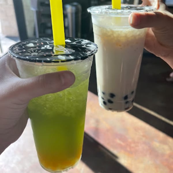 Two hands holding bubble tea drinks, one green and yellow, the other white with black tapioca pearls.